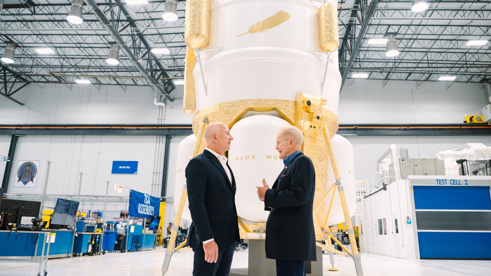 Two men in suits talking in front of a large spacecraft.