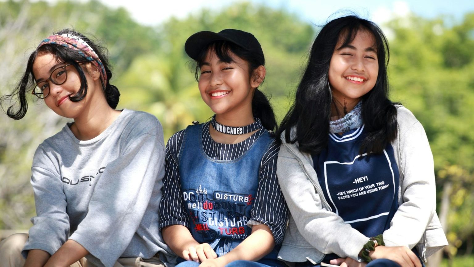 Three young girls sitting on a bench and smiling.