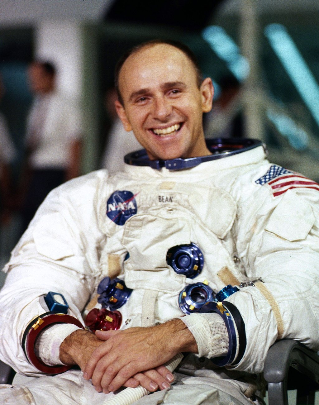 A man in a space suit smiling and sitting in a chair.