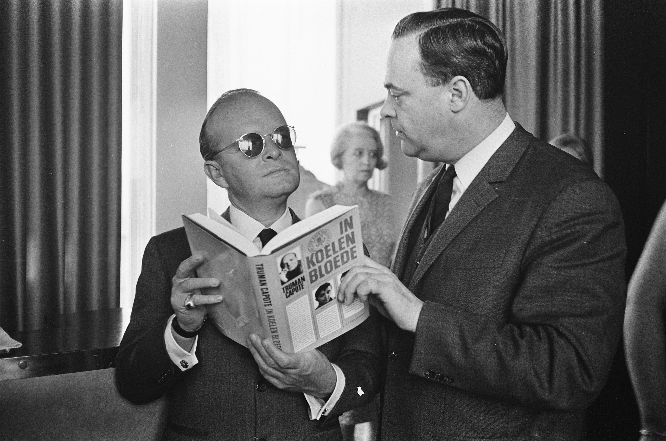 Two men in suits reading a book with an air of paranoia.