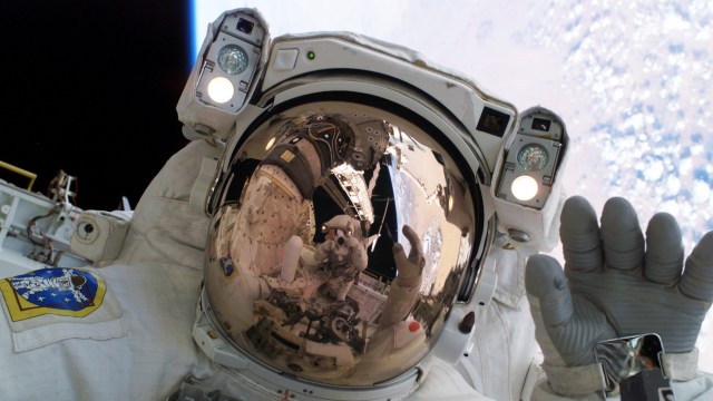 A man in an astronaut suit is waving to the camera, showcasing his leadership as he navigates outer space.