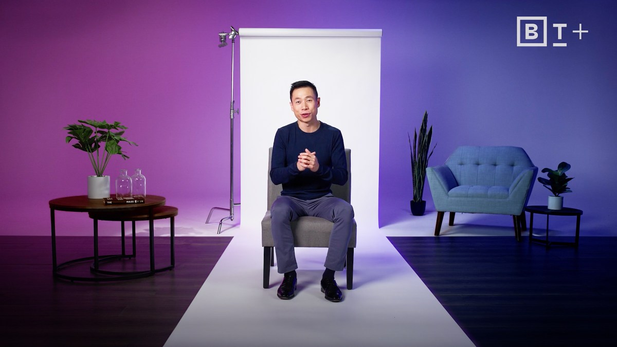Gorick Ng sitting on a chair in front of a purple background.