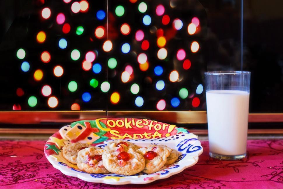 A plate of cookies and a glass of milk sit in front of a Christmas tree, creating a warm and inviting atmosphere.