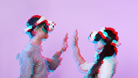 A man and woman wearing a vr headset and giving each other a high five.