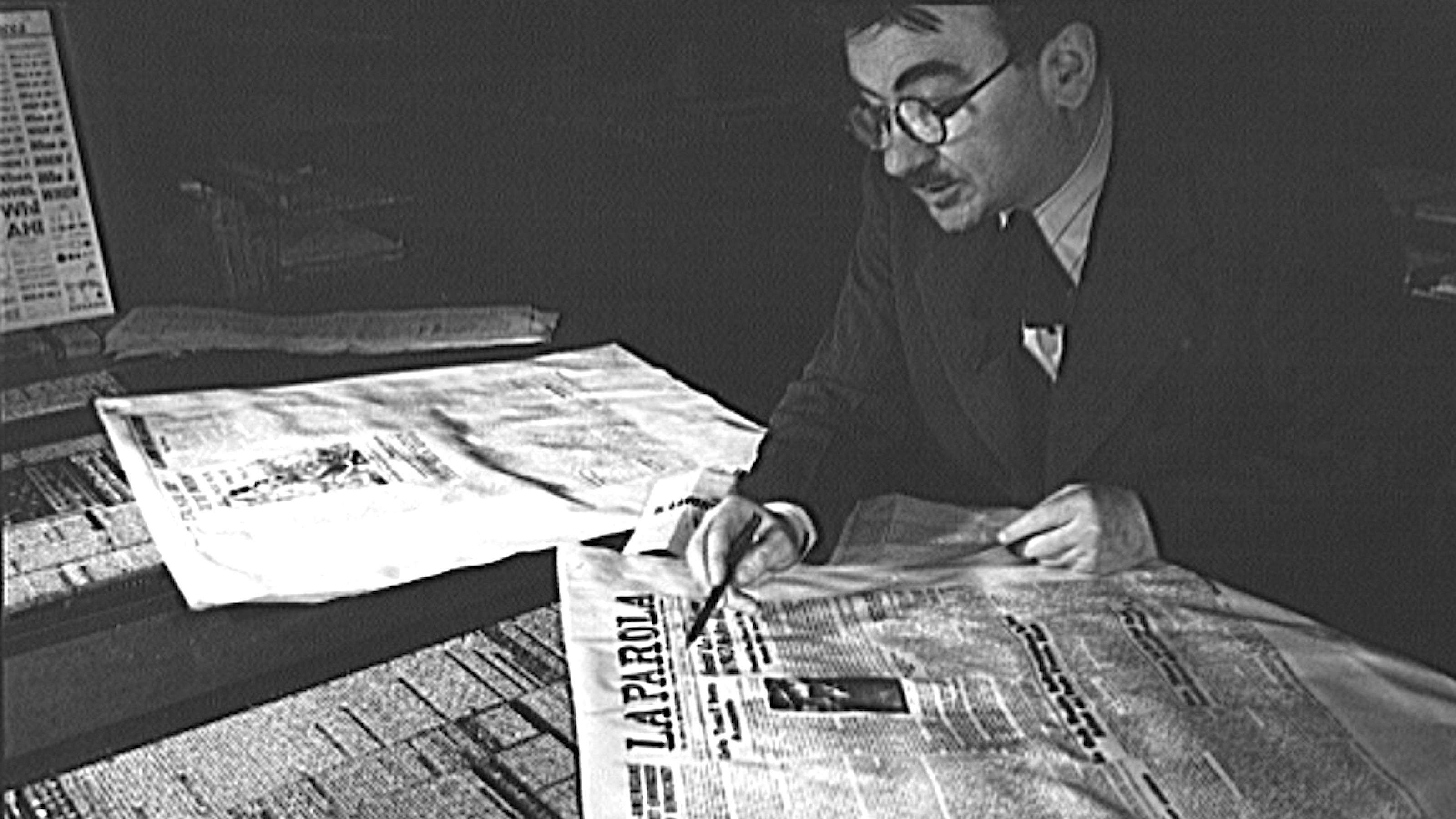 A man, engaged in the act of reading, is seated at a table with a newspaper in front of him.