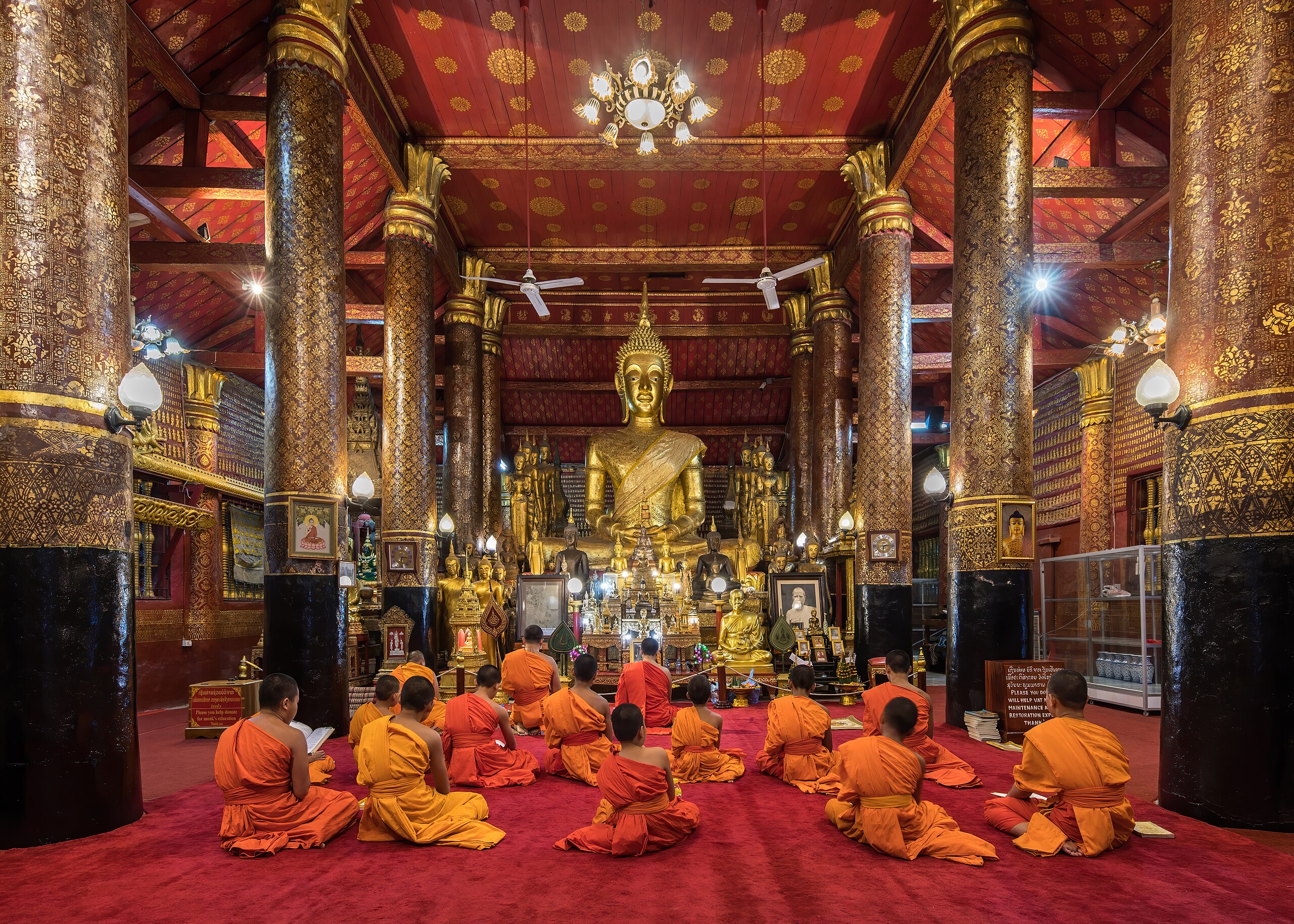 A group of monks sitting on the floor in front of a large Buddha, practicing Buddhism.