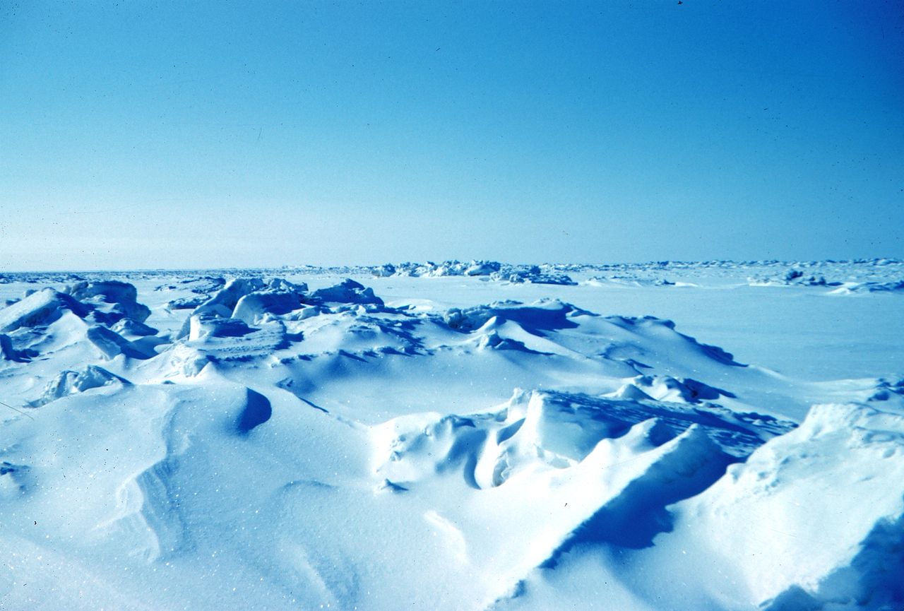 A large area of ice covered in snow with a blue sky.