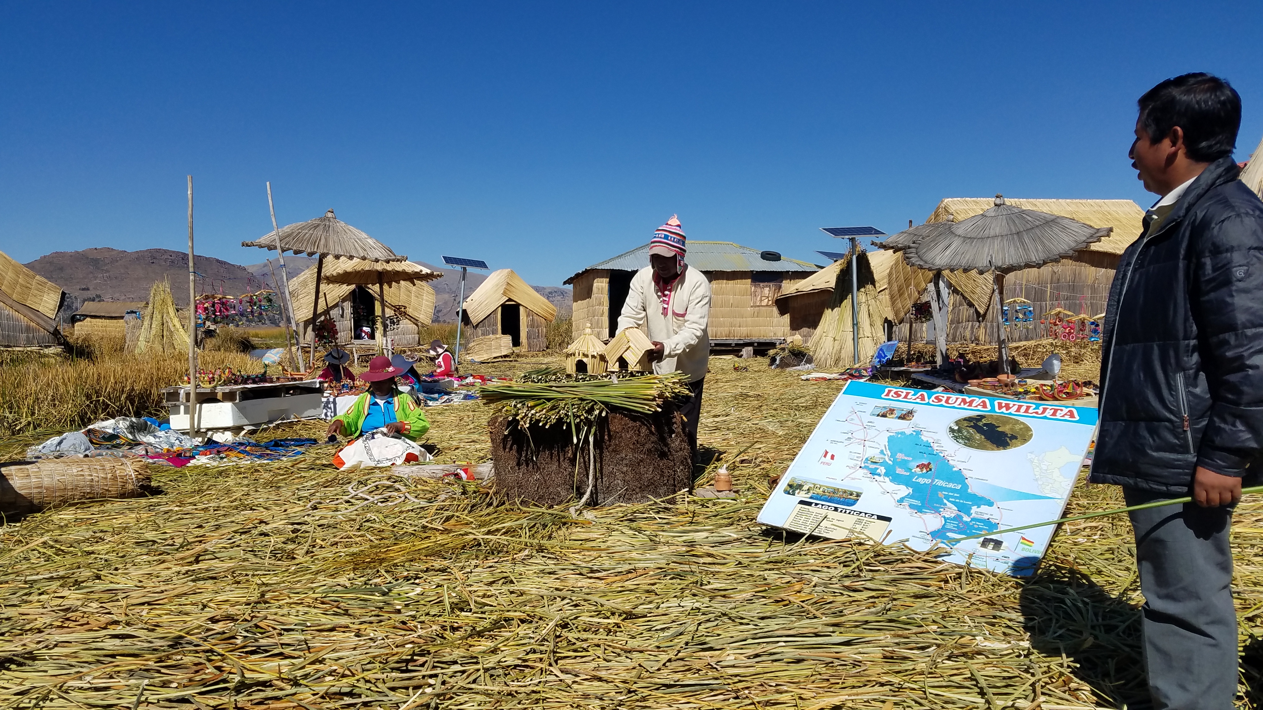 A Uros man in a hat and striped shirt working on a field with straw huts and a map.