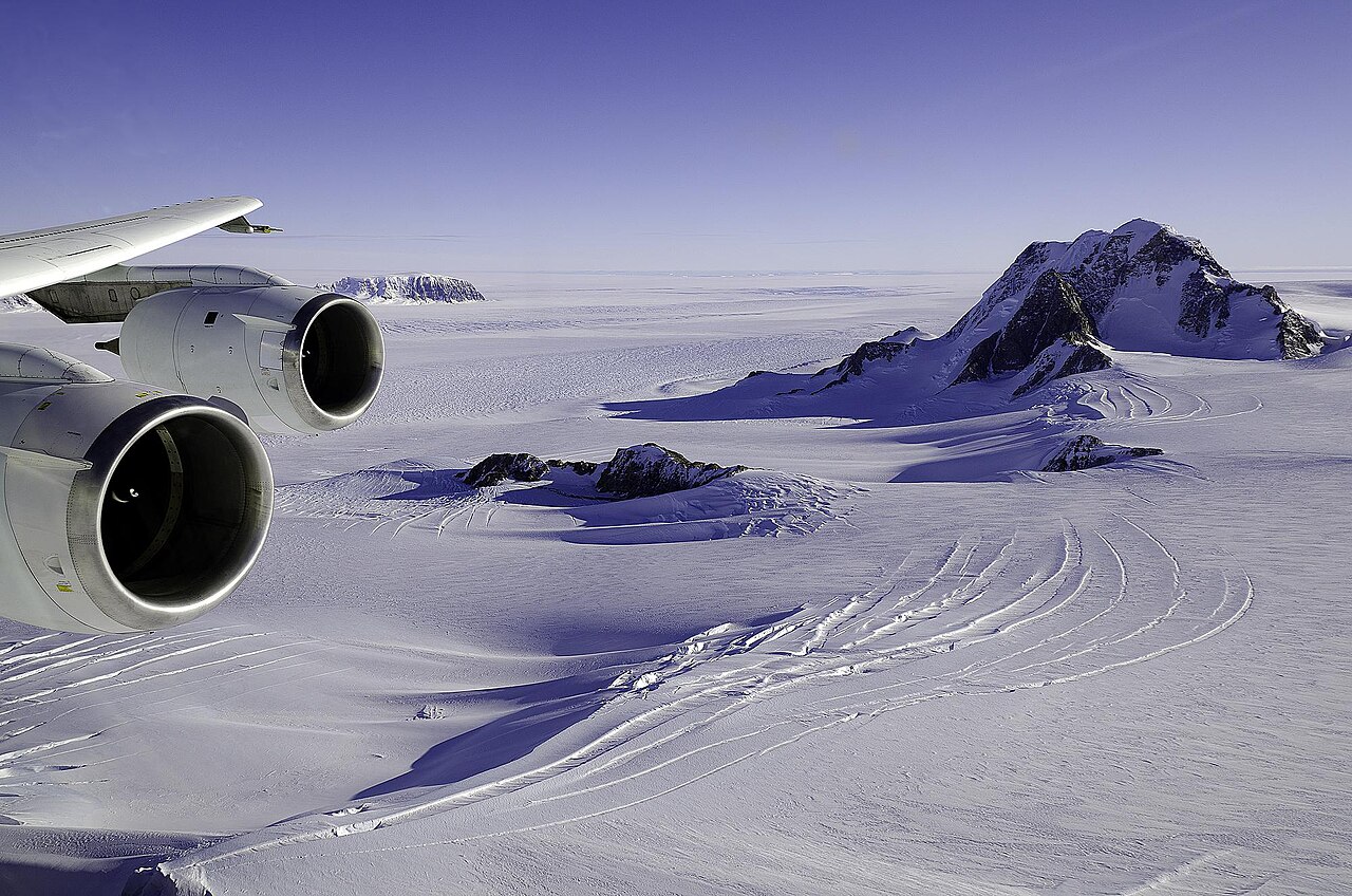 A plane flying over a snow covered landscape.
