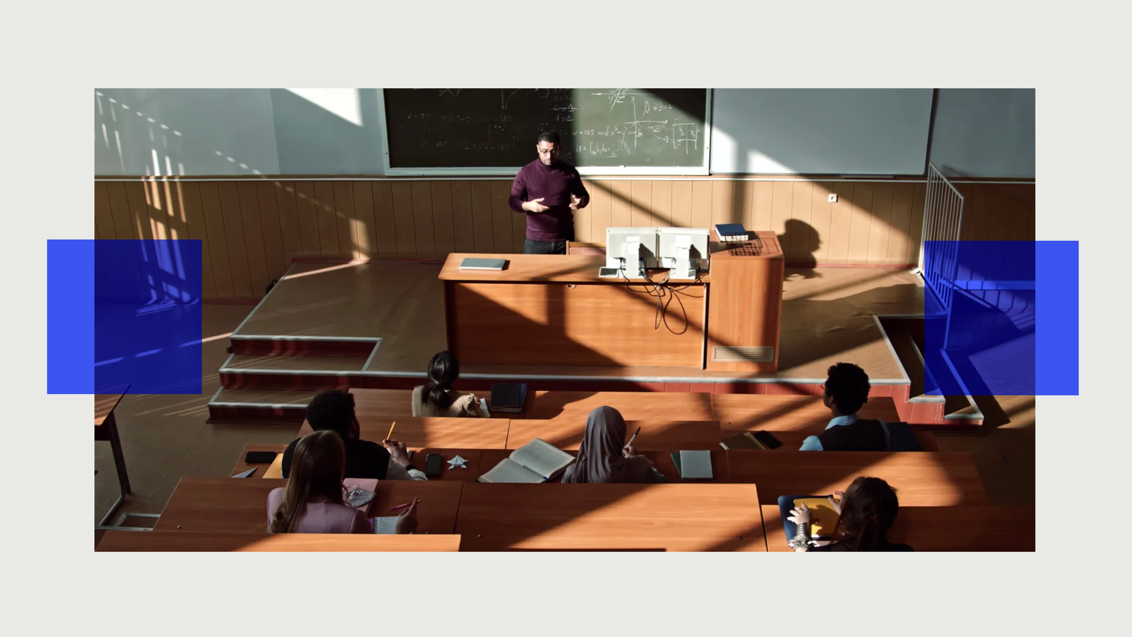 Lecturer standing in front of a classroom, teaching college admissions students seated at desks with sunlight casting shadows.