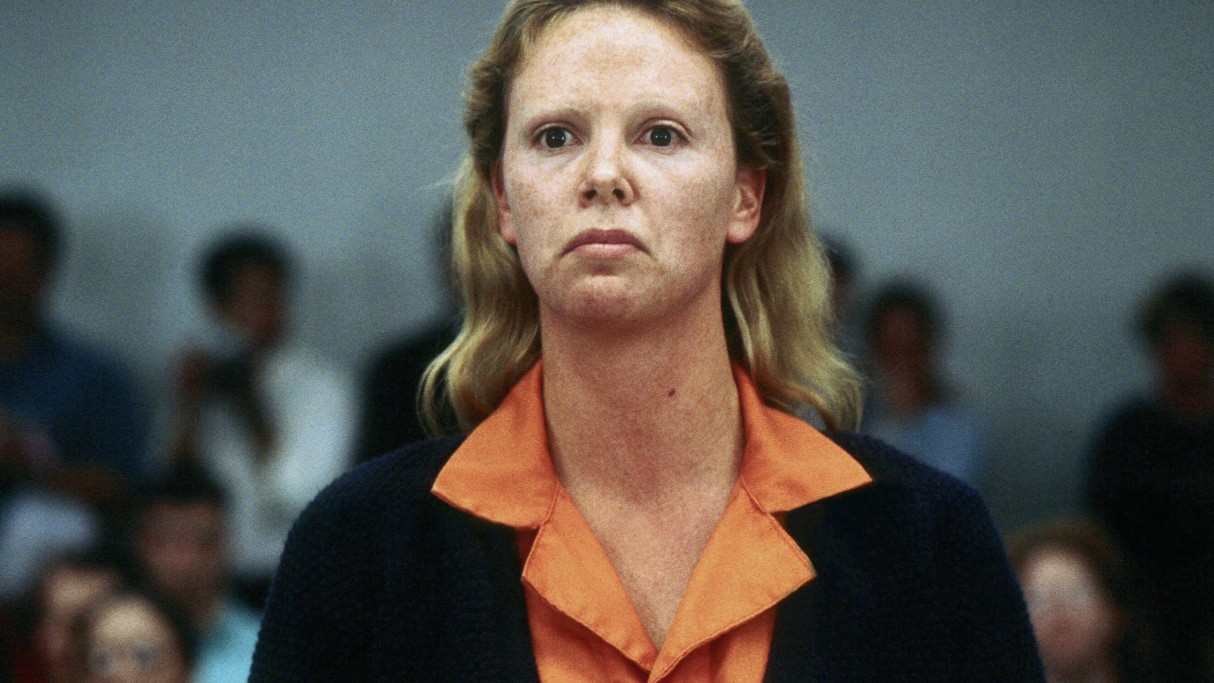 A woman in an orange shirt standing in front of a crowd.