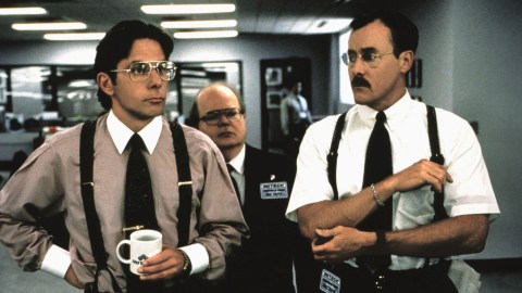 Two men in suspenders standing next to each other in an office, possibly enduring the presence of a bad boss.
