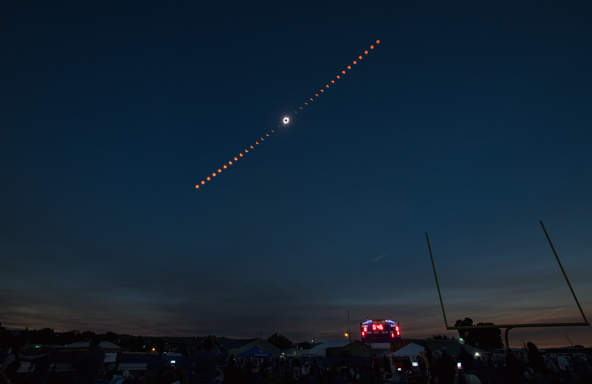 The phases of a total eclipse captured in sequence over a gathering of spectators.