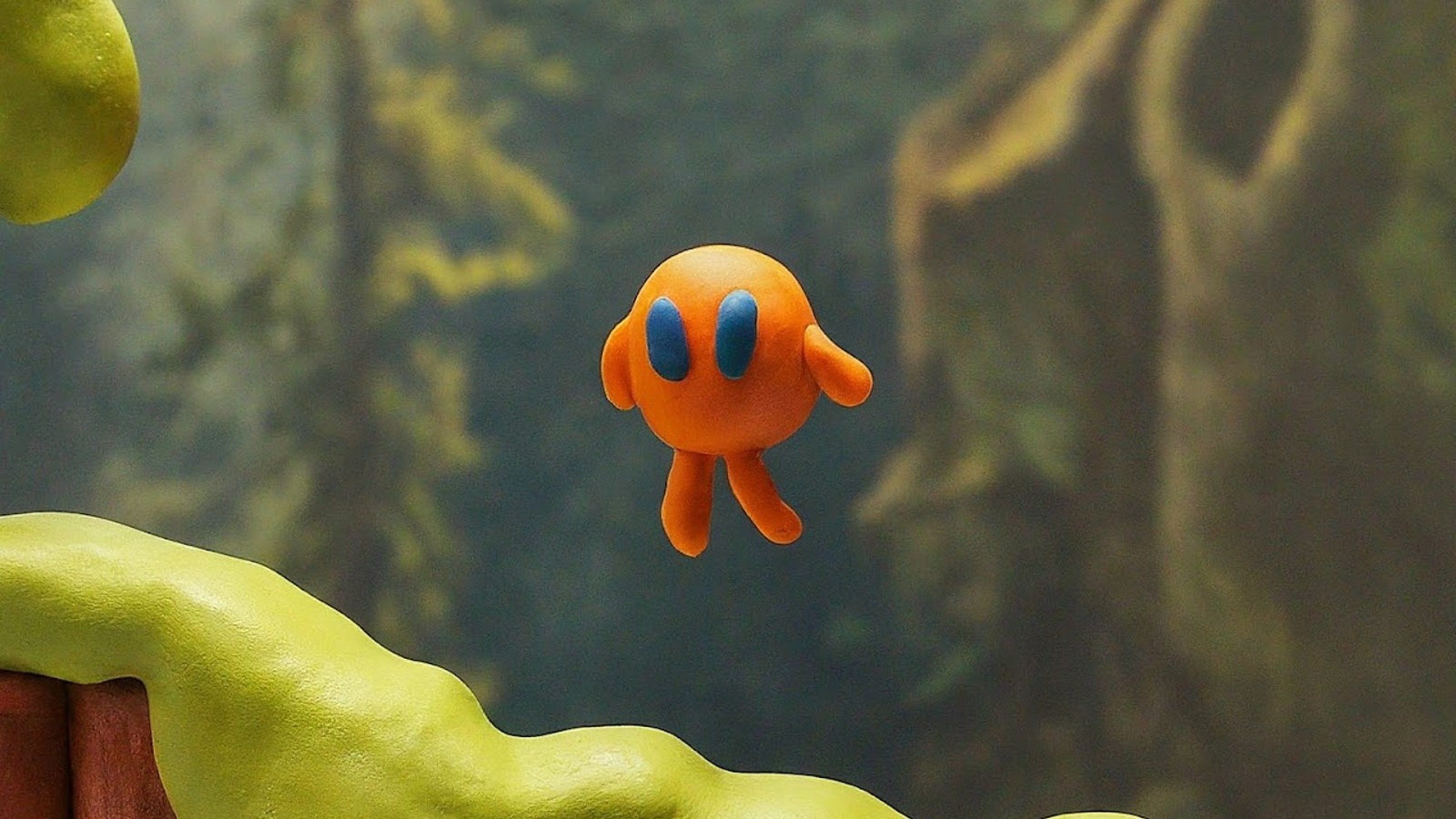Orange character with large eyes floating against a forest backdrop.