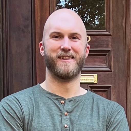 A bald man smiling in front of a door.