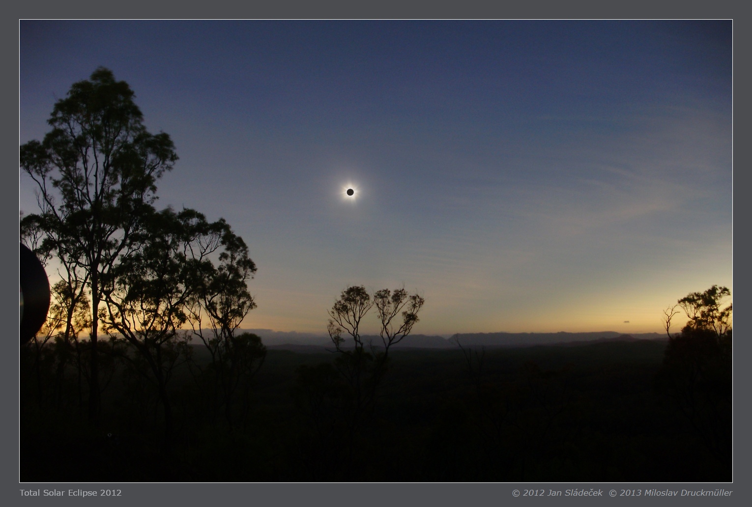 Total eclipse over a forested horizon at dusk.