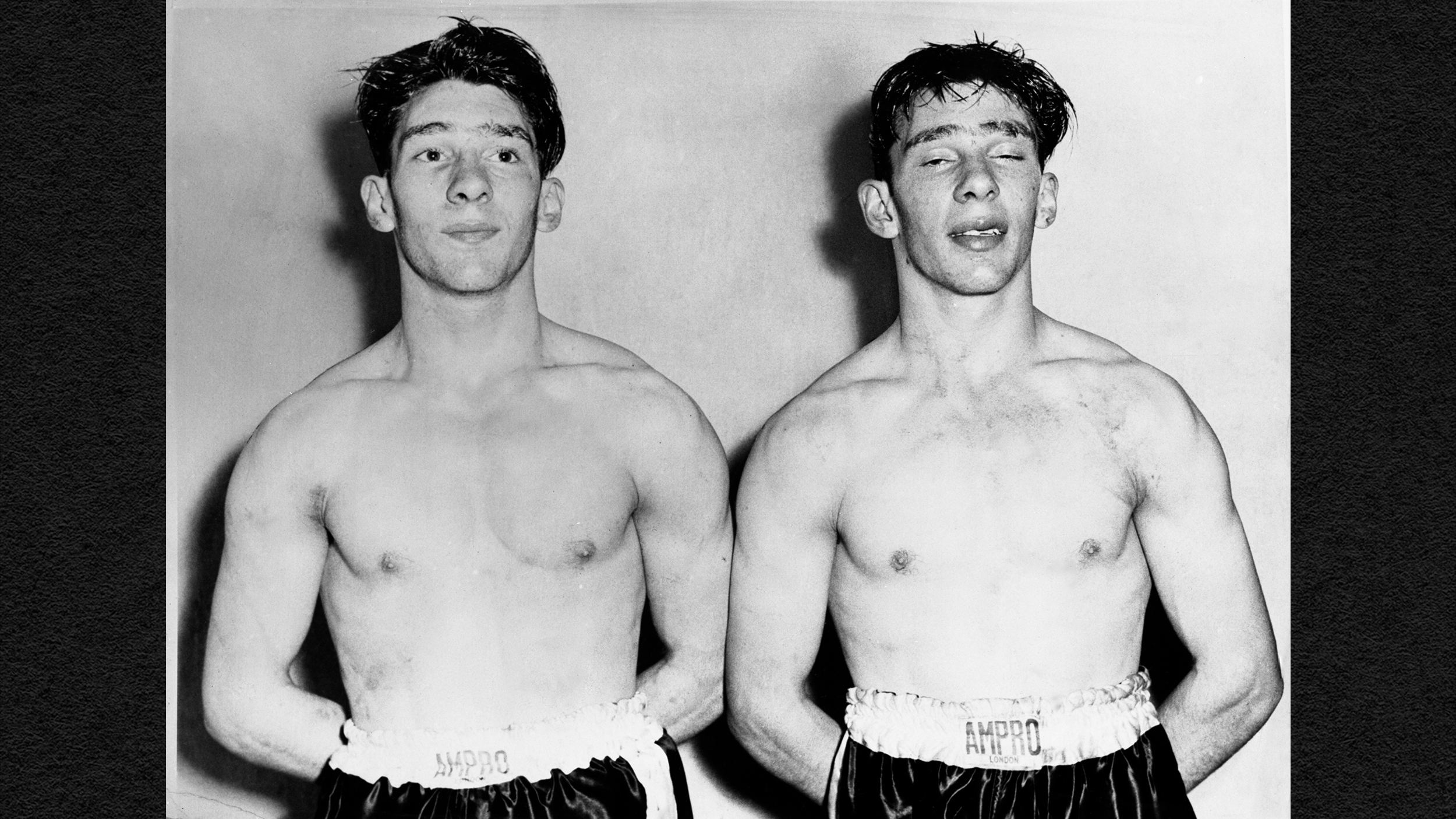 Two identical twin men in boxing gear standing next to each other.
