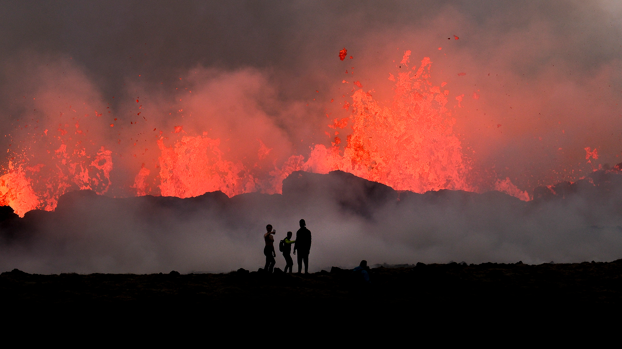 Spectators observing a dramatic eruption from active volcanoes at twilight.