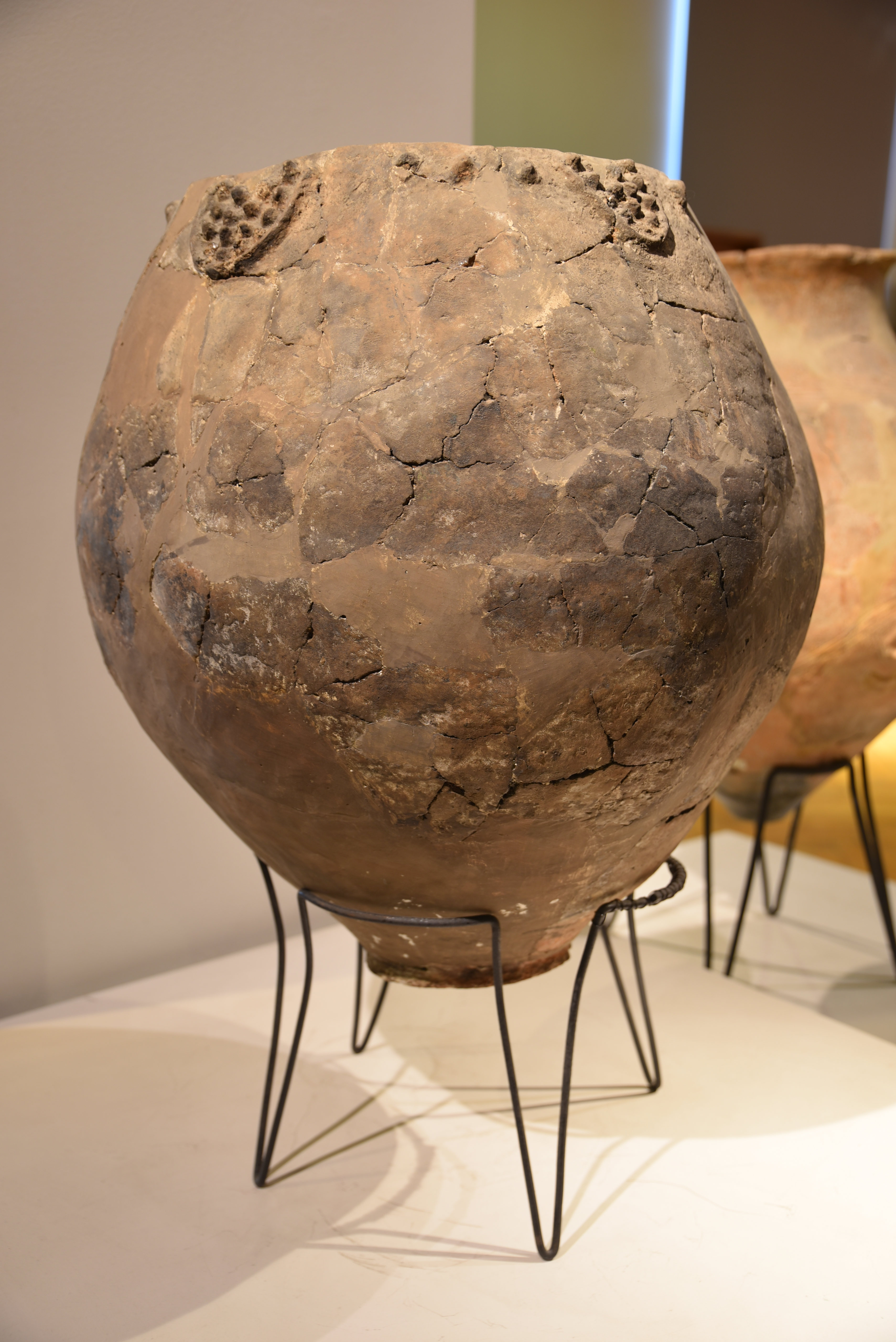 Large, ancient ceramic pot with cracks and restoration, displayed on a metal stand, embodying how humans transform the earth.