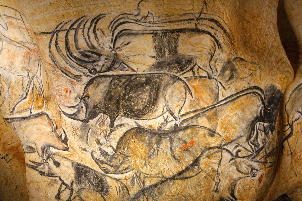 Prehistoric cave paintings, possibly created by early humans, depicting a herd of animals, possibly bison, on a rocky surface.