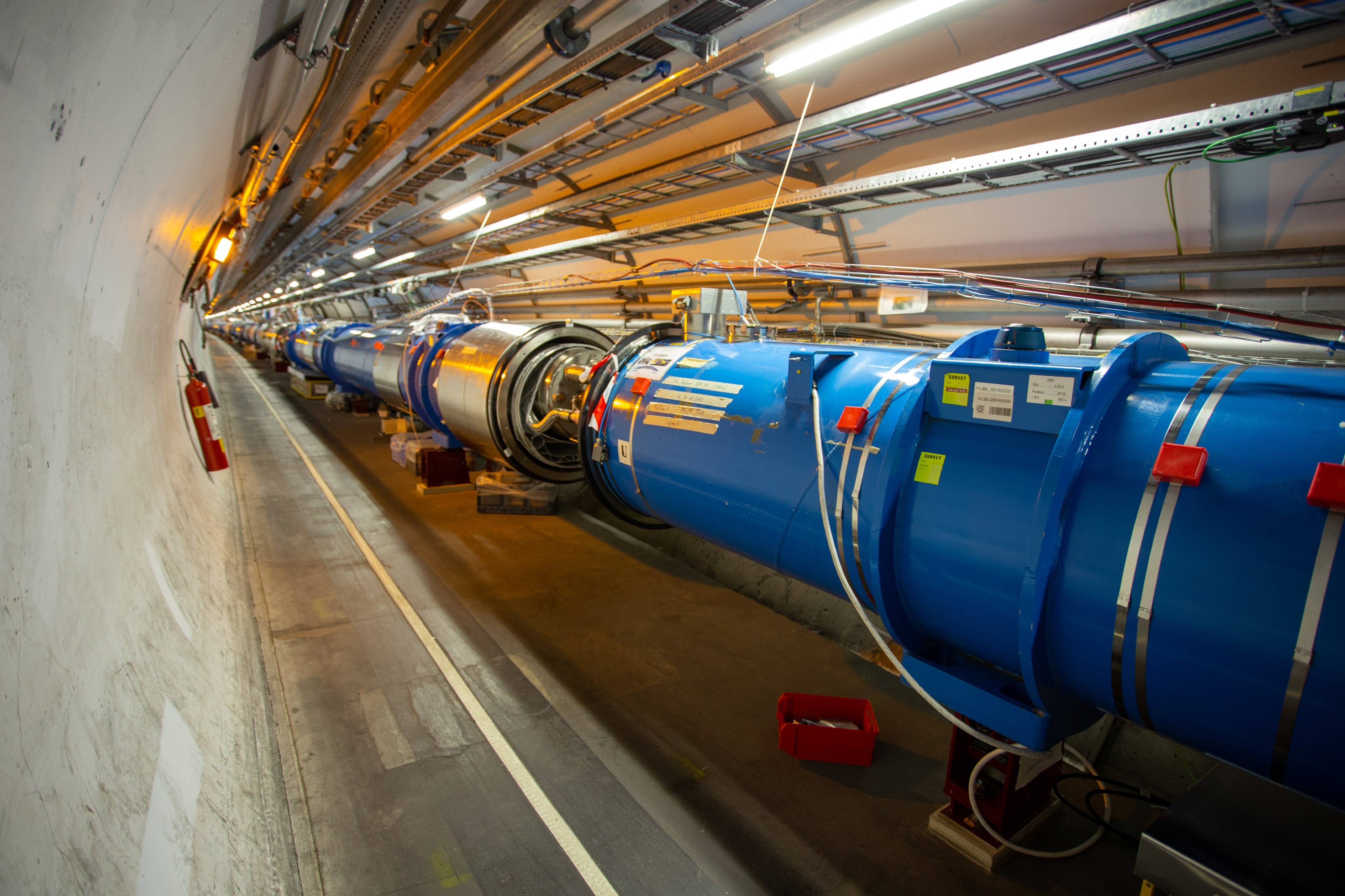 Section of the large hadron collider (lhc) tunnel with blue cylindrical superconducting magnets.