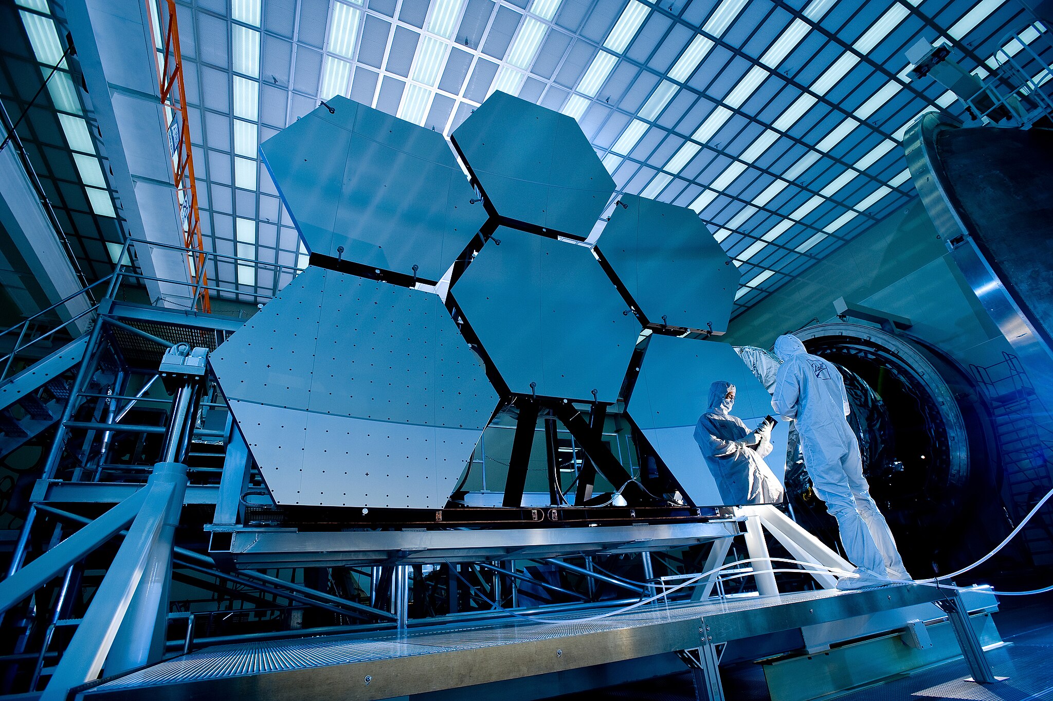 Engineers inspecting a large, segmented mirror of an astronomical telescope in a laboratory setting.
