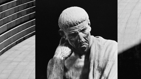Black and white image of a stone statue depicting an elderly man in thoughtful pose, positioned against geometric building lines, symbolizing generous leaders.