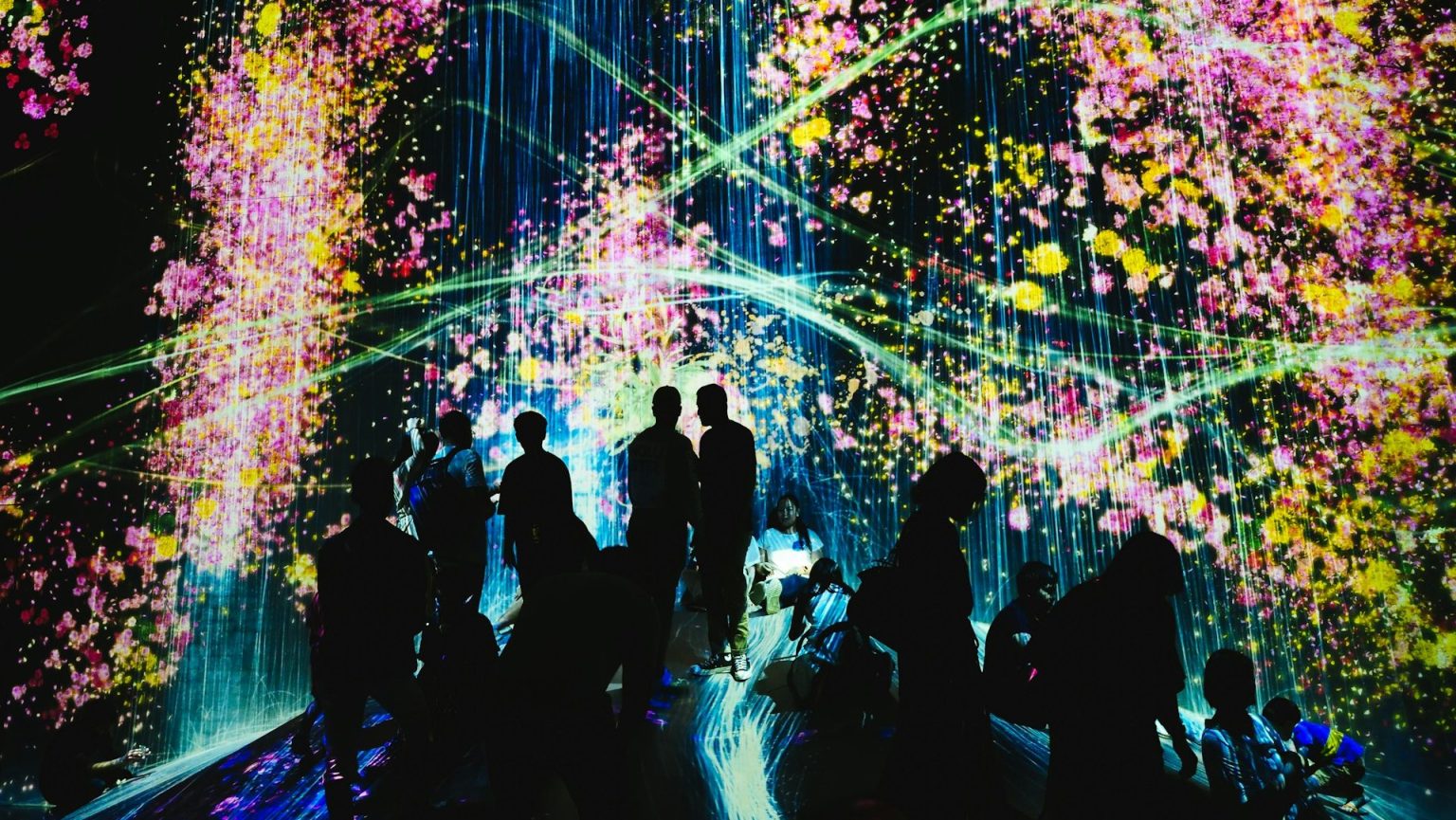 Silhouettes of posthumans immersed in a vibrant digital light display featuring floral patterns.
