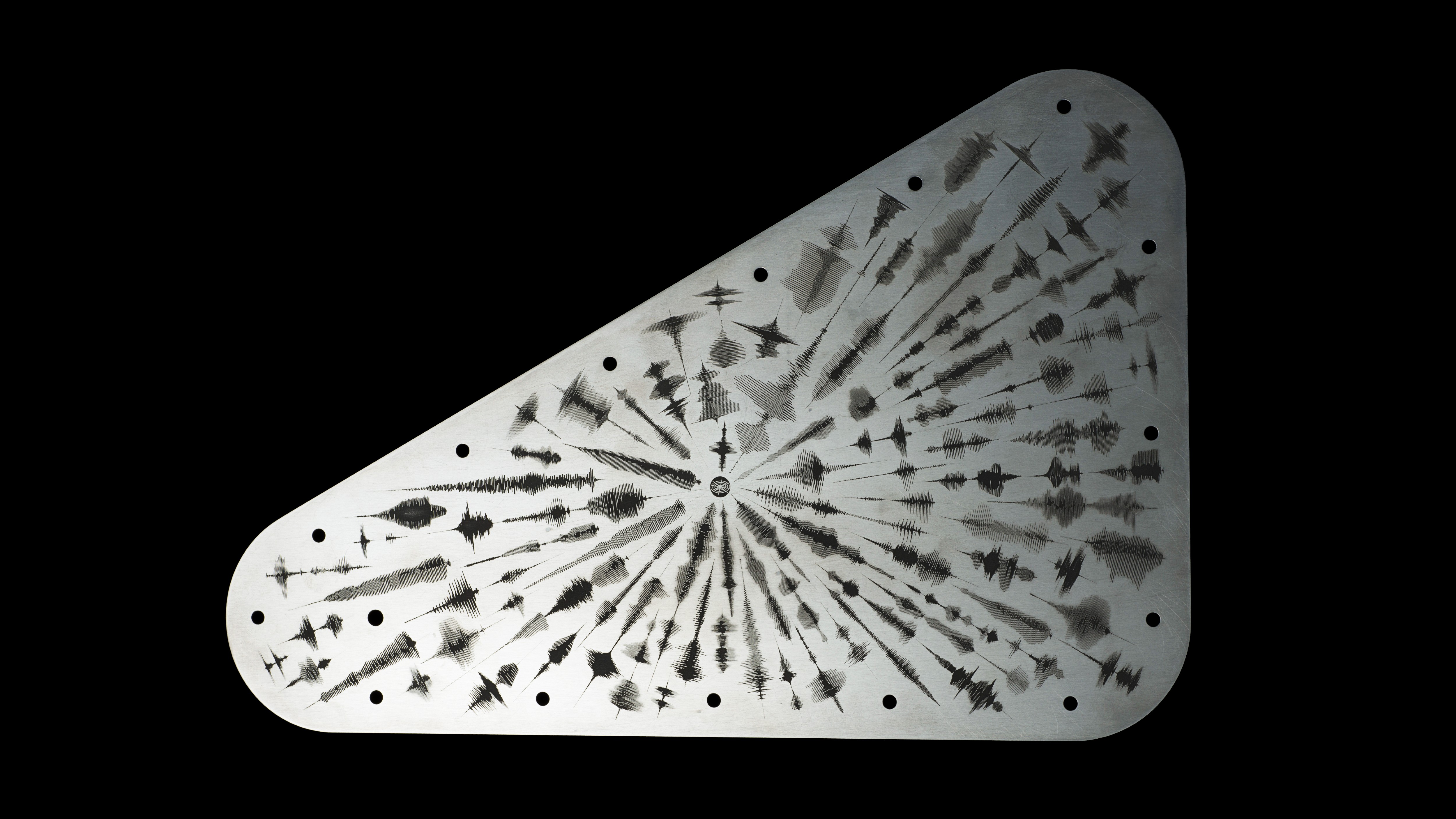 Triangular metal plate with radial pattern of drilled holes and engraved lines, creating a burst effect, isolated on black background.
