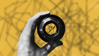 A hand holding a camera lens against a yellow background with shadow patterns, symbolizing problem-solving success.