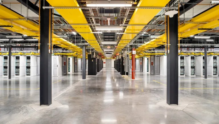 Interior of a large, modern data center with rows of yellow cable trays running above and sleek, polished floors.