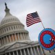 An American flag and a decorative shield with a peace symbol, evoking a sense of paranoia, in front of the United States Capitol building under a cloudy sky.