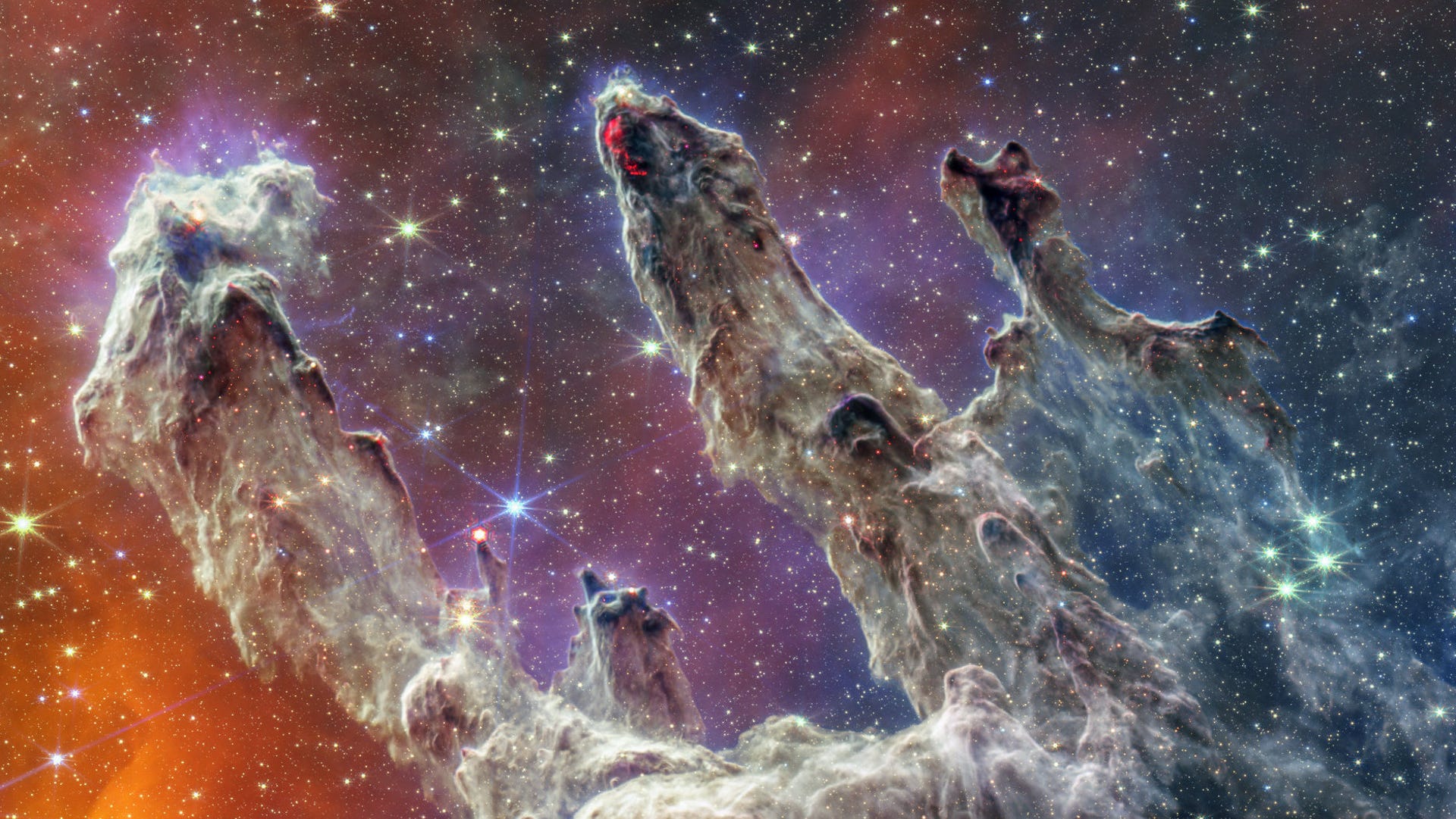 Colorful interstellar gas and dust form towering pillars in a star-forming region of space.