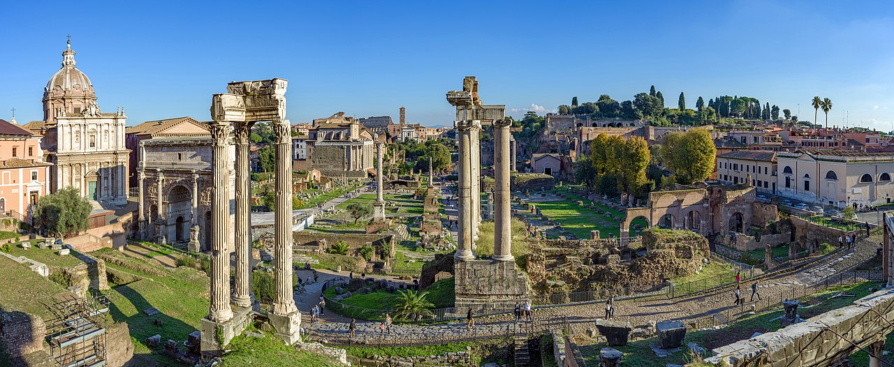 Panoramic view of the Roman Forum in Rome, featuring ancient ruins, columns, and historic buildings under a clear blue sky.