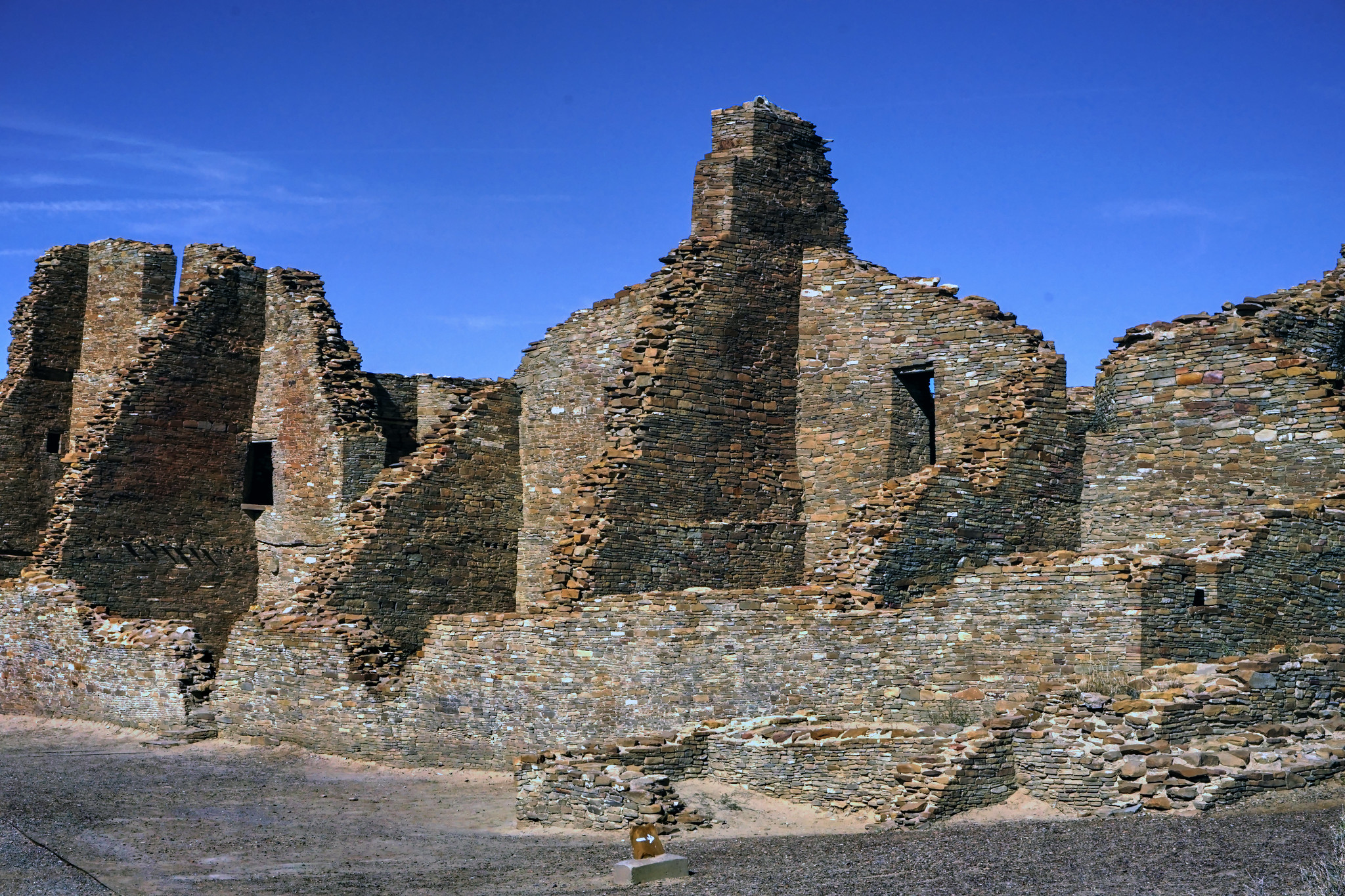 Ancient ruins of a large stone structure with partially intact walls against a clear blue sky.