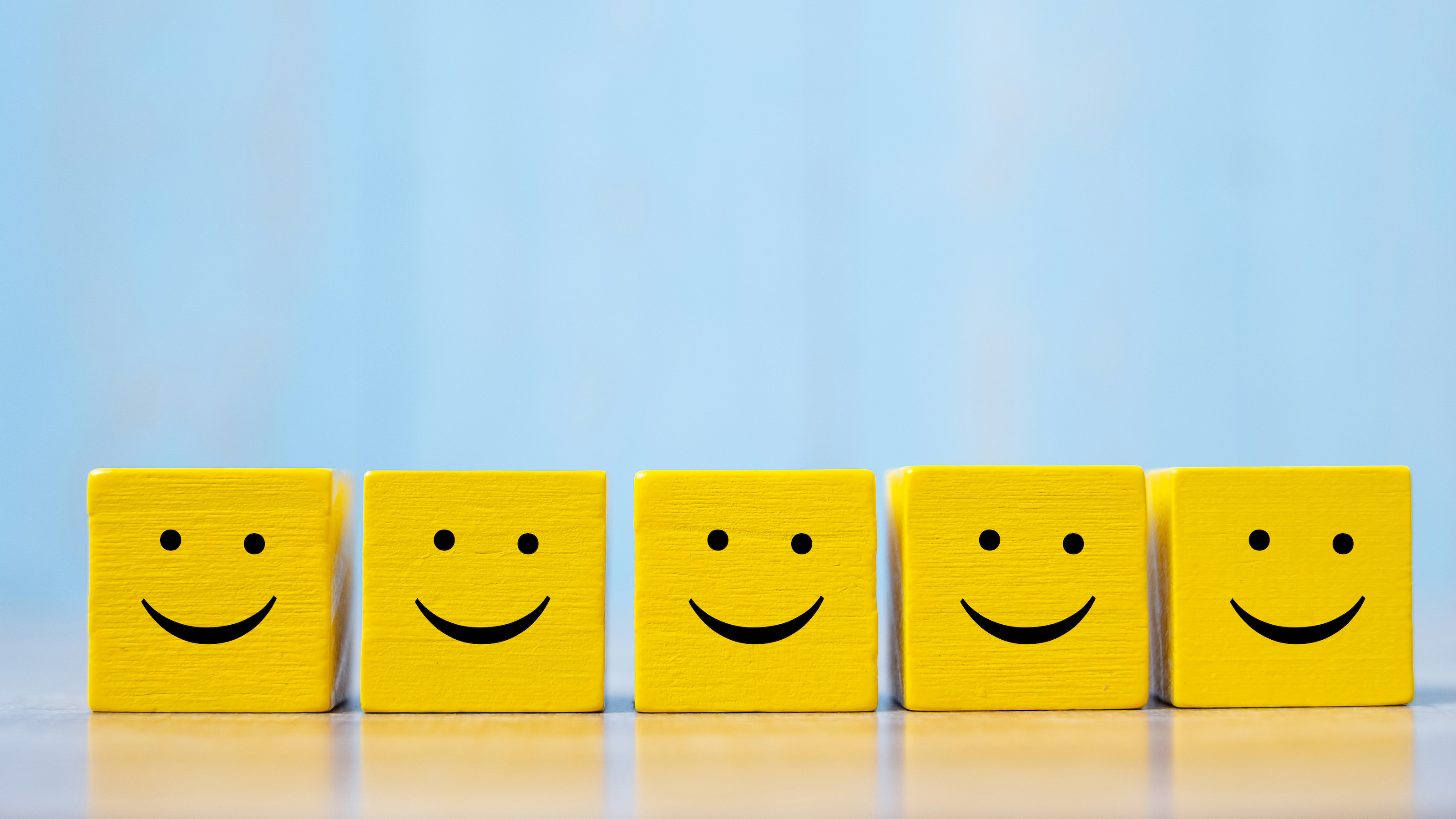Five yellow blocks with smiling faces, representing workplace happiness, aligned in a row against a blue background.