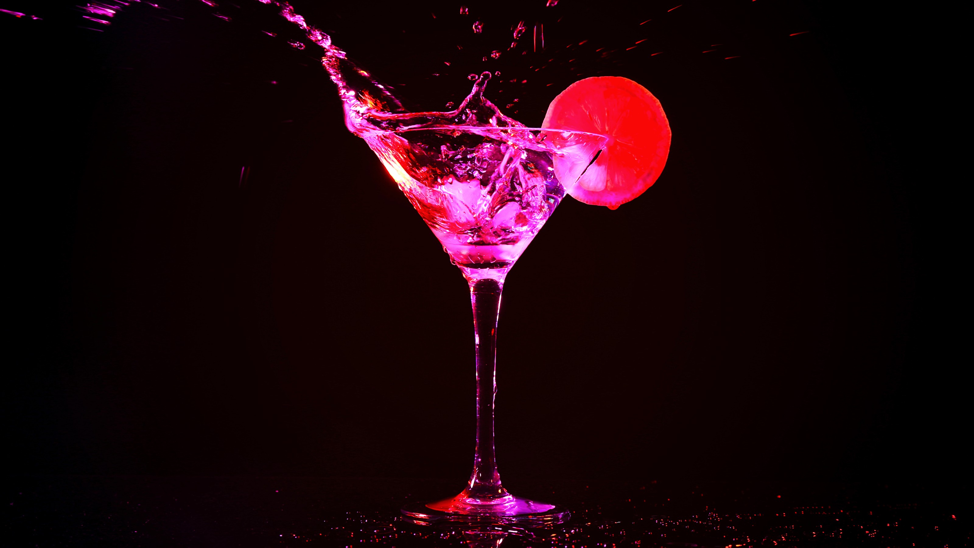 A splash of brightly colored liquid erupts from a martini glass garnished with a red citrus slice against a dark background, hinting at an unexpected hangover remedy.