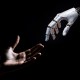 A robotic hand and a human hand reach towards each other against a dark background.