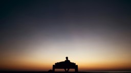 A person sitting on a bench silhouetted against a colorful sunset sky.