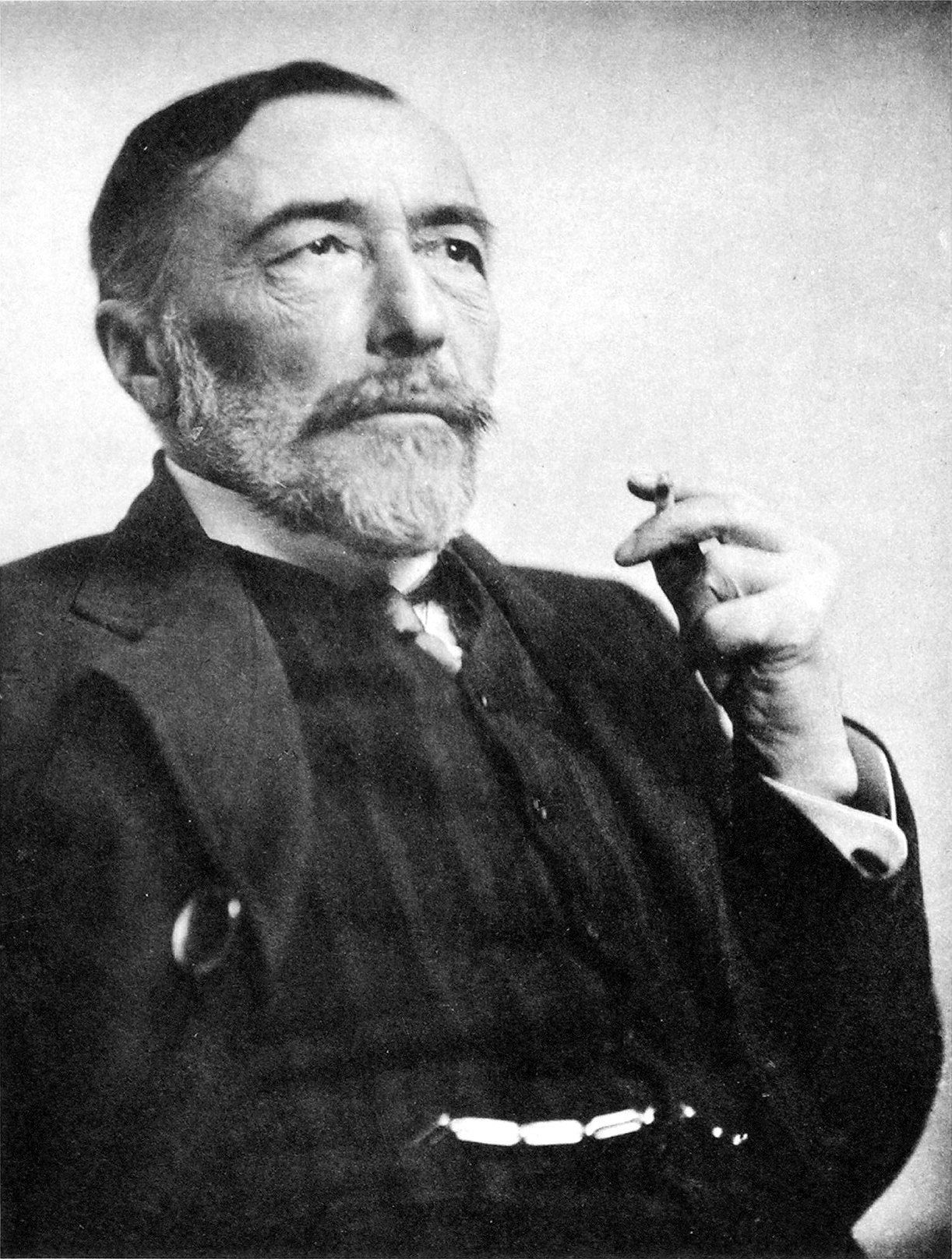 A black-and-white portrait of an older man with a beard, holding a monocle to his eye. He is dressed in a suit and looks off into the distance.