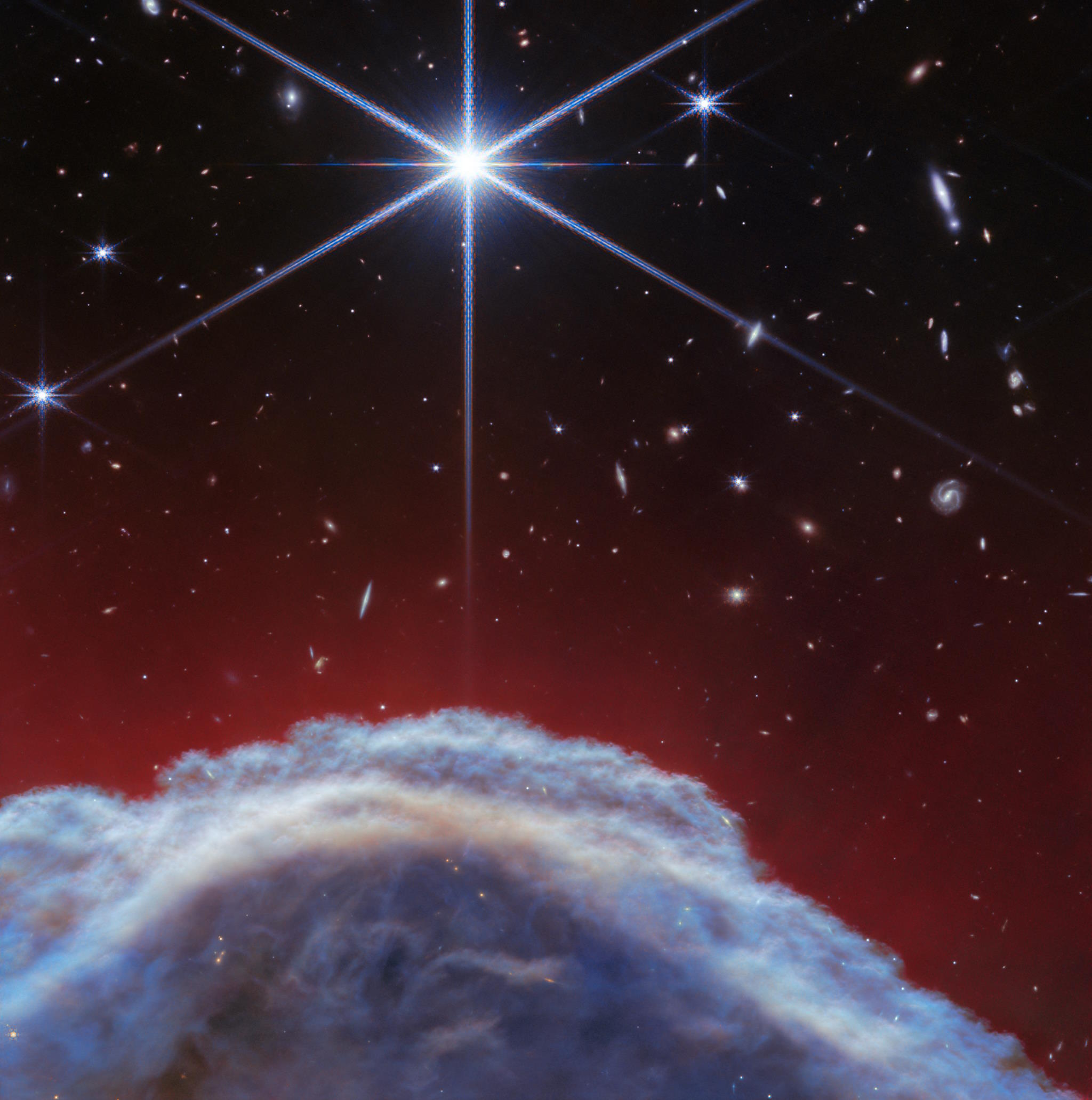 A celestial image captured by the JWST showing a bright star at the center with smaller stars and a vibrant, cloud-like Horsehead Nebula in the foreground against a deep red and black space background.