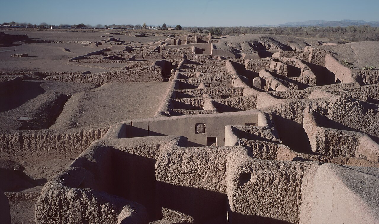An aerial view of adobe ruins in Paquimé, Mexico, showcasing ancient walled structures and pathways under a clear sky with distant mountains.