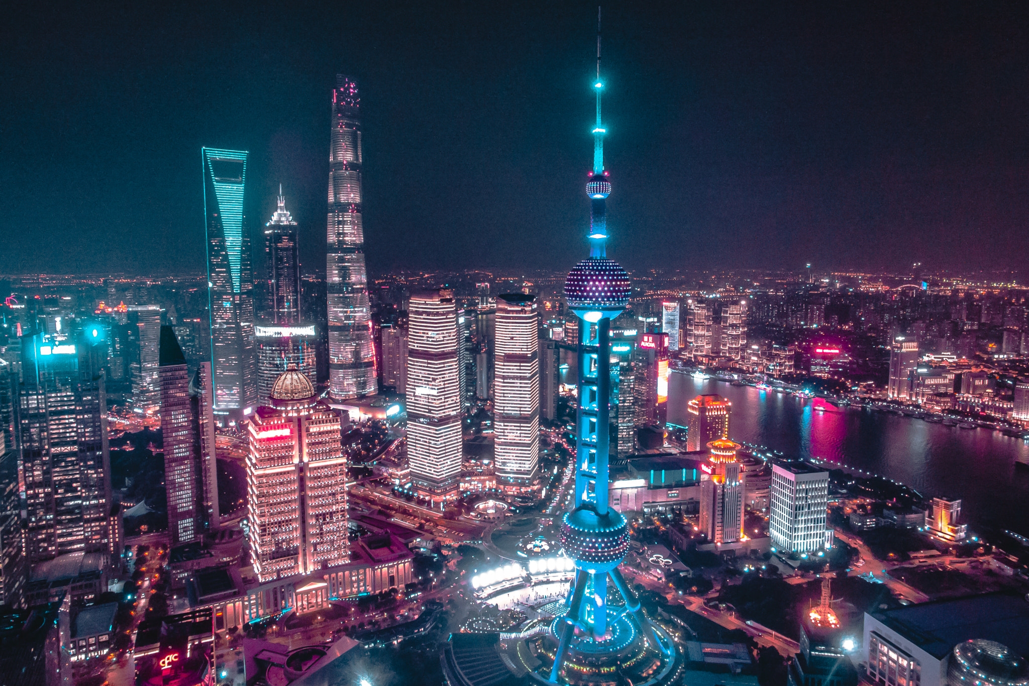 Aerial night view of Shanghai cityscape featuring brightly lit skyscrapers and the Oriental Pearl Tower with surrounding buildings illuminated.
