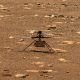 Nasa's ingenuity mars helicopter captured mid-flight on the martian surface, surrounded by rocky terrain.