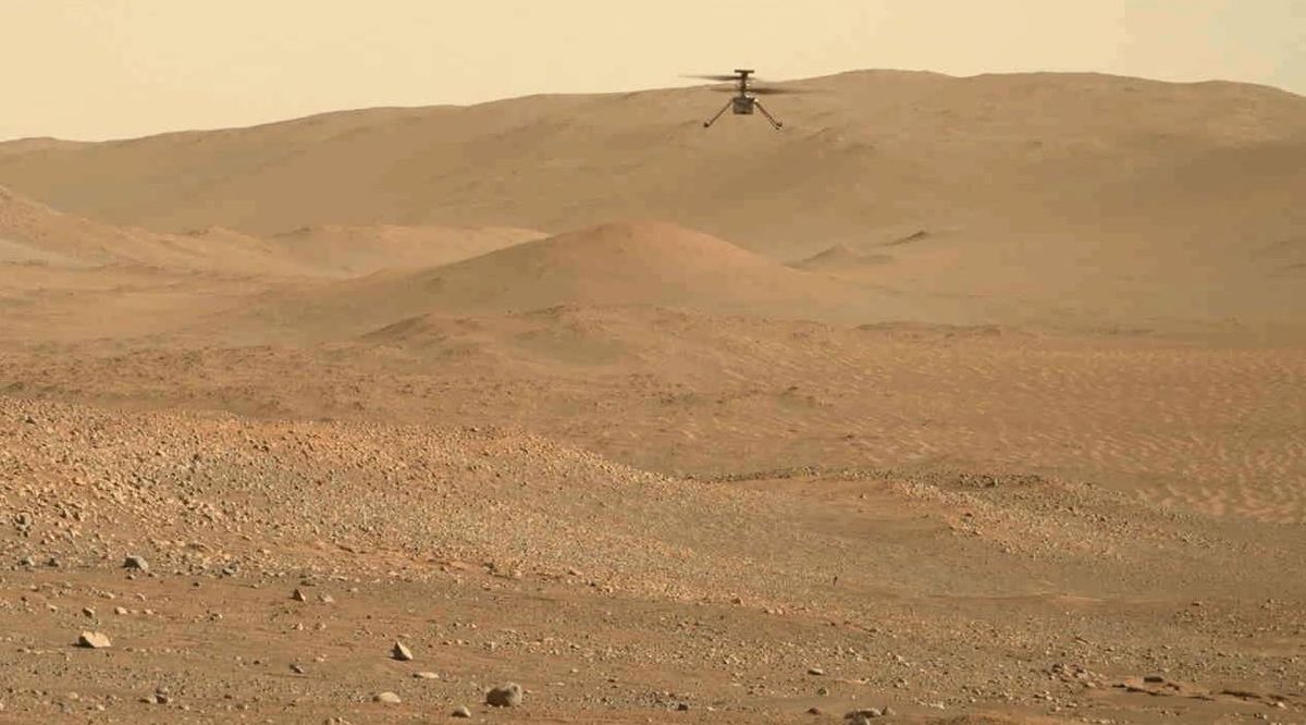 Nasa's ingenuity helicopter hovers above the martian surface, with arid terrain and small hills in the background.