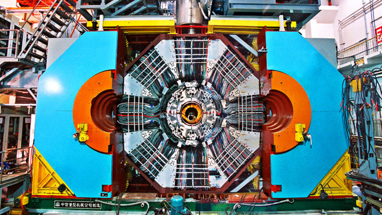 Front view of an open particle detector searching for glueball particles at a physics research facility, displaying intricate internal components and surrounded by structural supports.