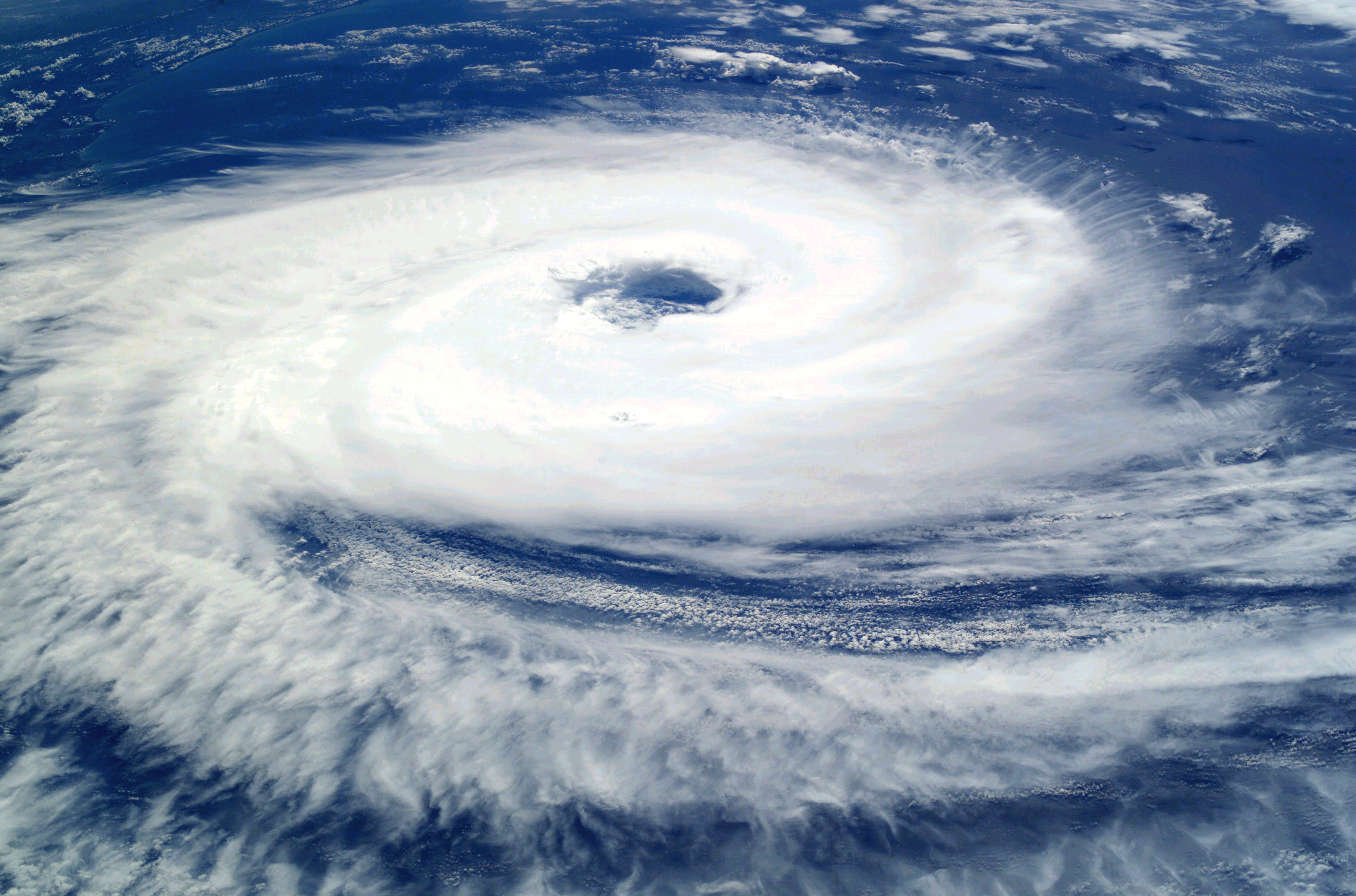 A satellite view of a large, swirling hurricane over the ocean with a clear eye in the center. The storm's dense cloud patterns are prominent against the blue water.