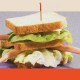 A sandwich with lettuce and bread, adorned with a toothpick, features doll arms and legs sticking out, creating a whimsical yet slightly eerie scene evoking playful hints of cannibalism.