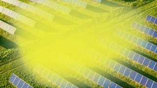 Aerial view of a solar farm with rows of solar panels installed on grassy fields on a sunny day.