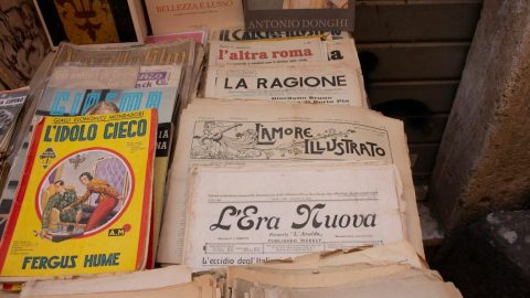 A display of vintage Italian newspapers and magazines, including "Cinema," "La Ragione," and "L'Era Nuova," arranged on a table at an outdoor market.